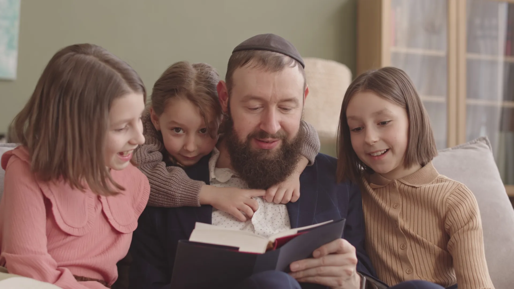 Jewish Father Reading Haggadah To His Three Little Daughters Celebrating Passover Seder At Home
